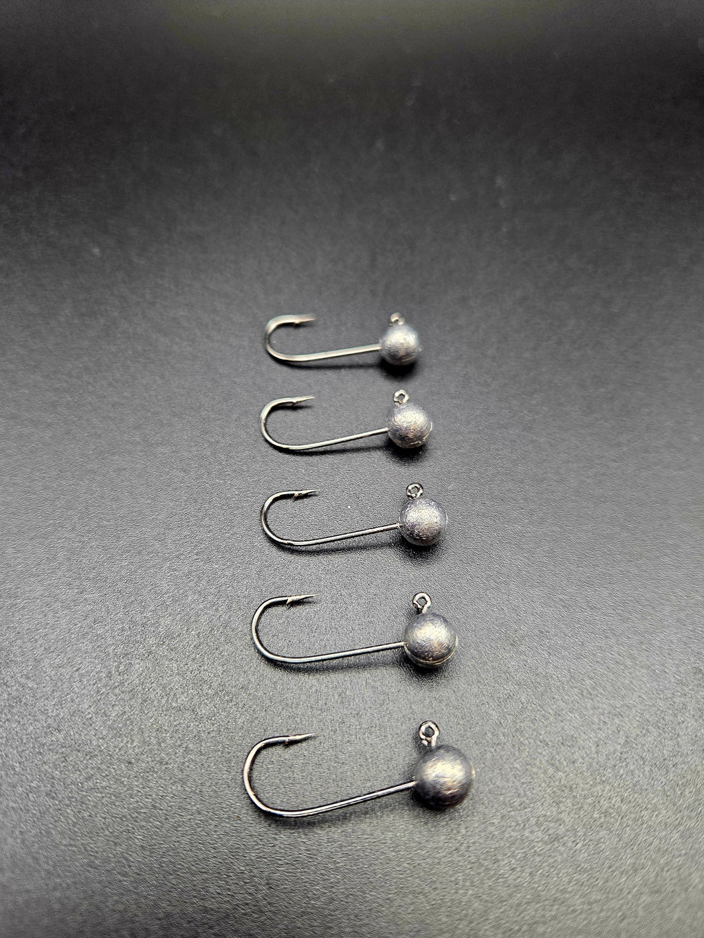 Five unpainted round-head micro jig heads arranged in a row on a dark background